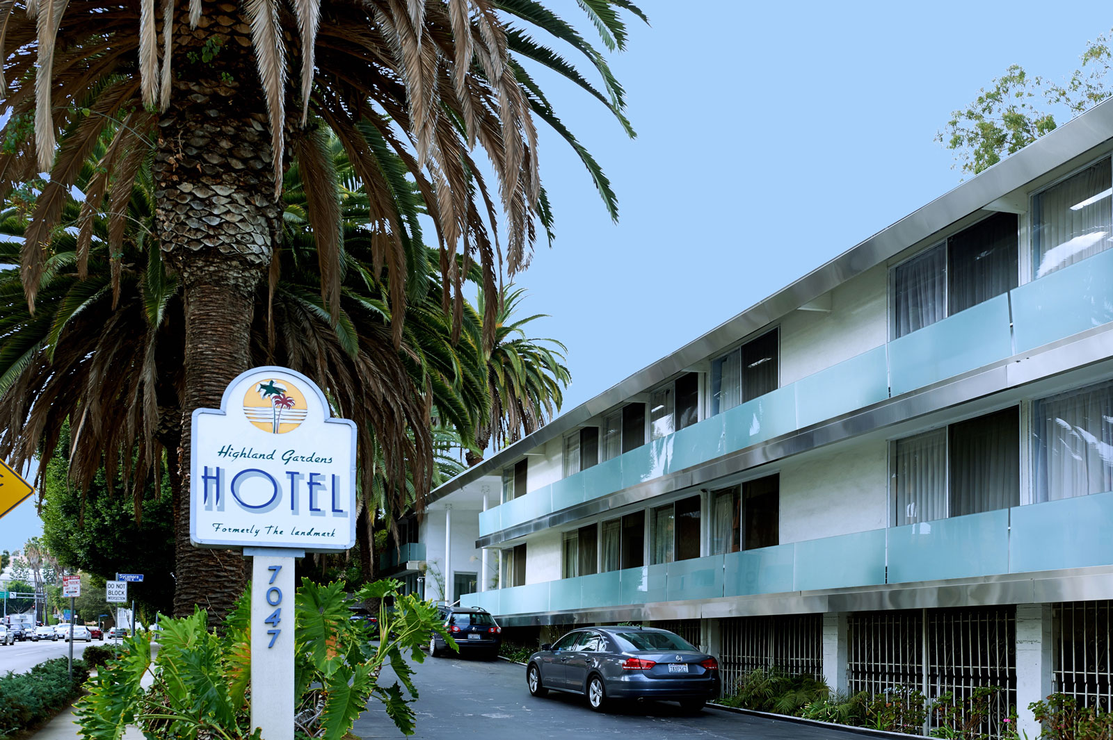 A photo of the exterior of a hotel with a sign and palm tree.